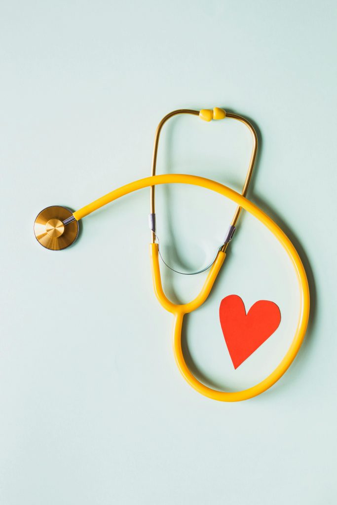 Yellow stethoscope arranged with a red heart cutout on a light green background, symbolizing heart health.